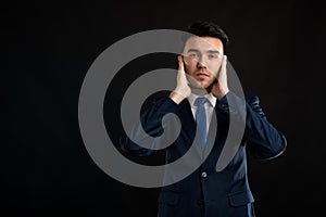 Portrait of business man wearing blue business suit and tie covering ears like deaf gesture