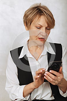 Portrait of business woman. Confident mature woman using mobile phone and typing on light gray background. Looking at