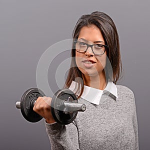 Portrait of business woman lifting weights against gray background