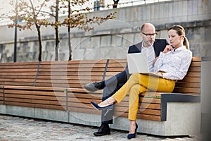 Portrait of businessman and businesswoman sitting on bench while discussing plans