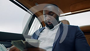 Portrait of businessman counting money at car. African guy smelling money at car