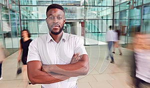 Portrait Of Businessman With Crossed Arms Standing In Lobby Of Busy Modern Office