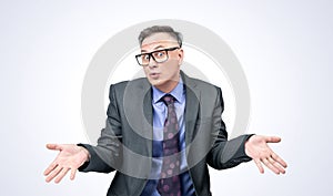 Portrait of a businessman in a dark suit and glasses who shrugs and spreads his arms showing empty palms. On a light background