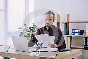 portrait of businessman doing paperwork at workplace with laptop