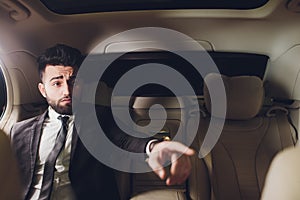 Portrait of businessman driving in car and smiling on his morning commute to work. Young man his finger pointing towards