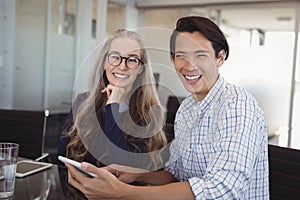 Portrait of businessman holding digital tablet with female colleague at desk