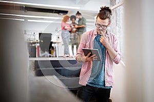 Portrait of businessman holding tablet in office and colleagues discussing in background