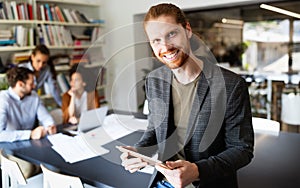 Portrait of businessman holding tablet in office and colleagues discussing in background