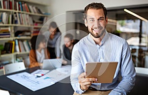 Portrait of businessman holding tablet in office and colleagues discussing in background