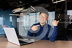 Portrait of businessman with laptop inside office, man smiling and looking at camera pointing with hands and finger
