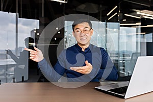 Portrait of businessman with laptop inside office, man smiling and looking at camera pointing with hands and finger