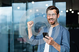 Portrait businessman in office, the man is looking at the camera with a smartphone and celebrating the victory, the man