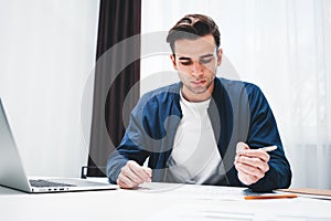 Portrait of businessman sitting at table use laptop and notepad in office space