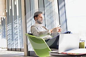 Portrait of Businessman sitting while using smartphone and drinking coffee in office lobby