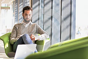 Portrait of Businessman sitting while using smartphone and drinking coffee in office lobby