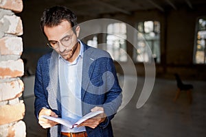 Portrait of businessman standing at the wall in empty room, making notes, working on new company opening