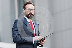 Portrait of businessman with tablet in hand on background of office building. Businessman using tablet outdoor with 4G.