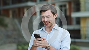 Portrait businessman using smartphone. Man typing messages on phone outside