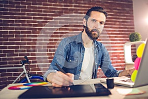 Portrait of businessman writing on graphic tablet while using laptop