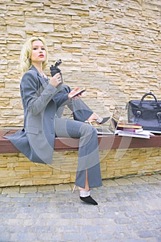 portrait of a businesswoman in a business suit with a phone in her hands. a woman is sitting on a bench with a laptop