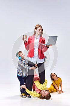 Portrait of businesswoman with laptop and little children playing around her with noise against grey studio background