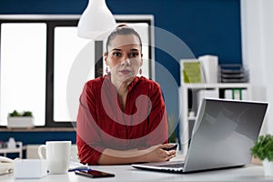 Portrait of businesswoman with laptop sitting at desk in startup office.