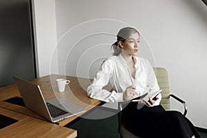 Portrait of a businesswoman with a laptop writing on a document in her office. Girl close-up at work.