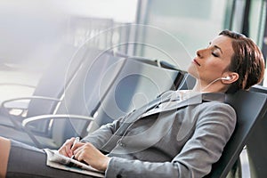 Portrait of businesswoman listening to music on smartphone while sleeping and waiting for boarding in airport