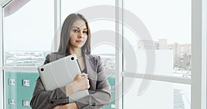 Portrait of businesswoman with notebook. Beautiful female executive standing near window at office