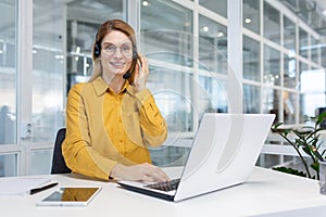 Portrait businesswoman, office worker looking at camera and smiling, using headset and laptop for remote online