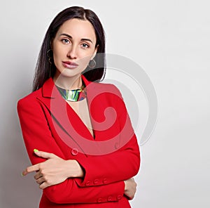 Portrait of businesswoman with permanent makeup in red jacket and modern jewelry standing with arms crossed at chest