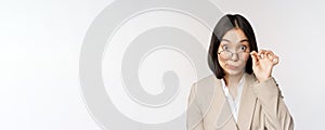 Portrait of businesswoman take-off glasses and looking surprised at camera, standing over white background