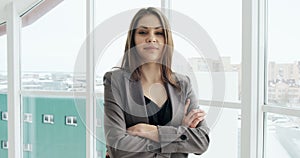 Portrait of businesswoman who crossing her arms and smiling. Beautiful female executive standing near window at office