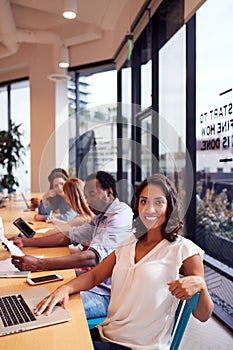Portrait Of Businesswoman Working At Desk In Shared Open Plan Office Workspace