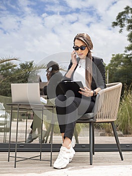 Portrait of busy Business Woman talking on cellphone and working on laptop. sitting outdoor in cafe