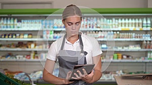 Portrait of a busy female sales assistant in a grocery typing on the digital tablet while taking inventory