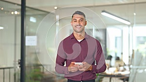 Portrait of busy latin business man standing in office using mobile phone.