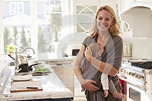 Portrait Of Busy Mother With Baby In Sling At Home
