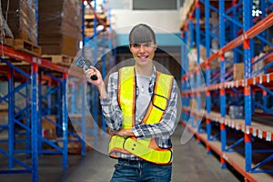Portrait of Cacuasian warehouse worker hold barcode scaner and smile also look at camera stay on way between shelves in workplace
