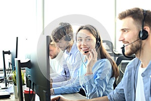 Portrait of call center worker accompanied by her team. Smiling customer support operator at work.