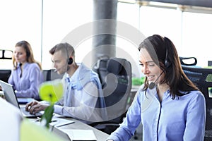 Portrait of call center worker accompanied by her team. Smiling customer support operator at work.