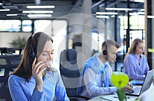 Portrait of call center worker accompanied by her team. Smiling customer support operator at work