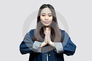 Portrait of calm beautiful brunette asian young woman in casual blue denim jacket with makeup standing with palm hands and yoga