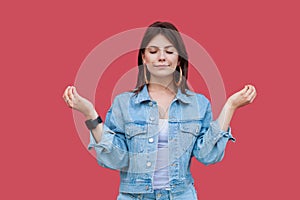 Portrait of calm beautiful brunette young woman with makeup in denim casual style standing with raised arms and doing meditating