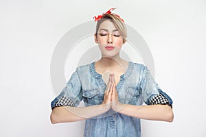 Portrait of calm beautiful young woman in casual blue denim shirt with makeup and red headband standing with palm hands and