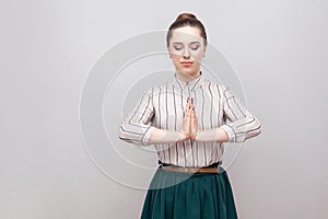 Portrait calm of beautiful young woman in striped shirt, green skirt with makeup and collected ban hairstyle, standing with closed