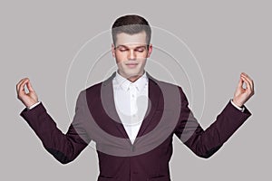 Portrait of calm handsome young man in violet suit and white shirt, standing, raised arms, closed eyes with yoga gesture and