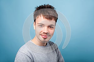 Portrait of calm positive young brunette man looking at camera with friendly expression. indoor studio shot isolated on blue