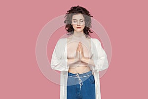 Portrait of calm relaxed beautiful brunette young woman with curly hairstyle in casual style standing palm hands and doing yoga