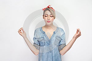 Portrait of calm relaxed beautiful young woman in casual blue denim shirt with makeup and red headband standing with raised arms